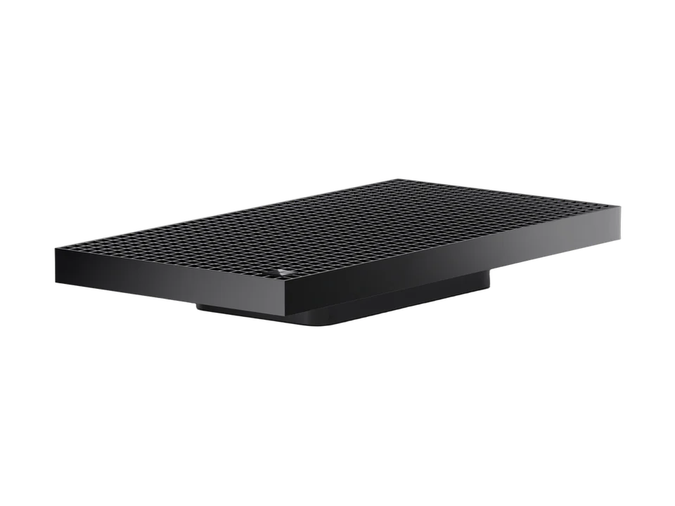Mini-PC Microsoft Surface RTX Spark Dev Box vu de trois quarts : boîtier noir plat au dessus en grille à carreaux, posé sur un socle en retrait, petit logo sur un coin.